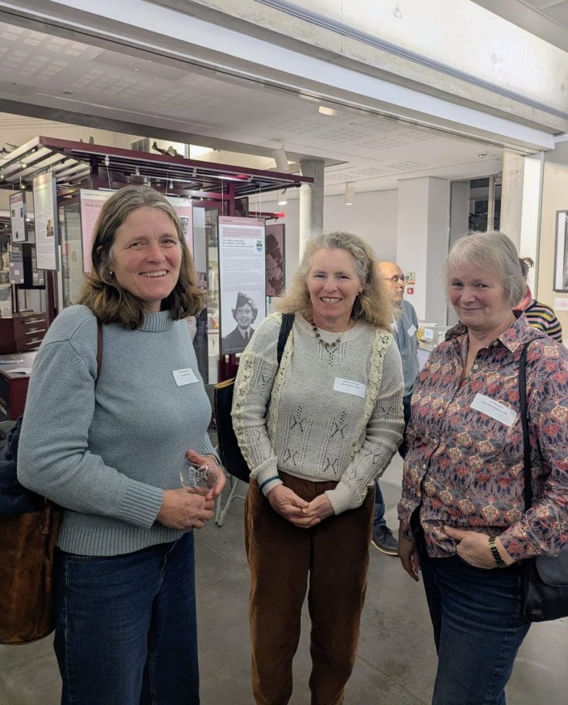 Three women smiling and posing together indoors at an event