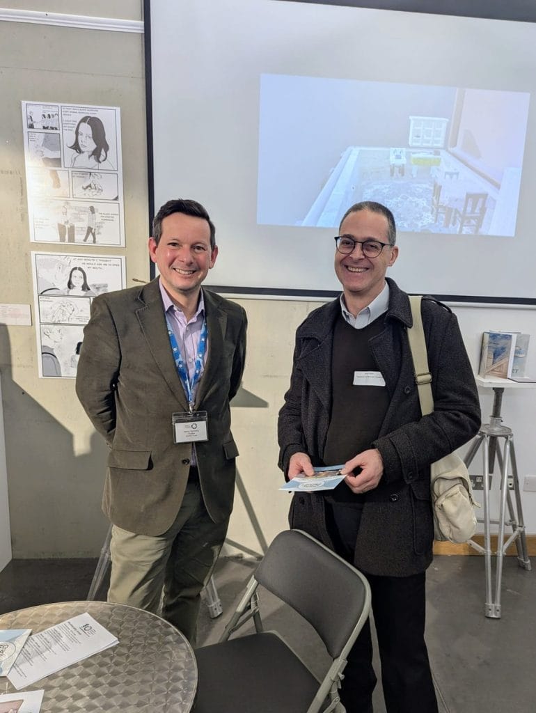 Two men wearing name badges standing together at a presentation event