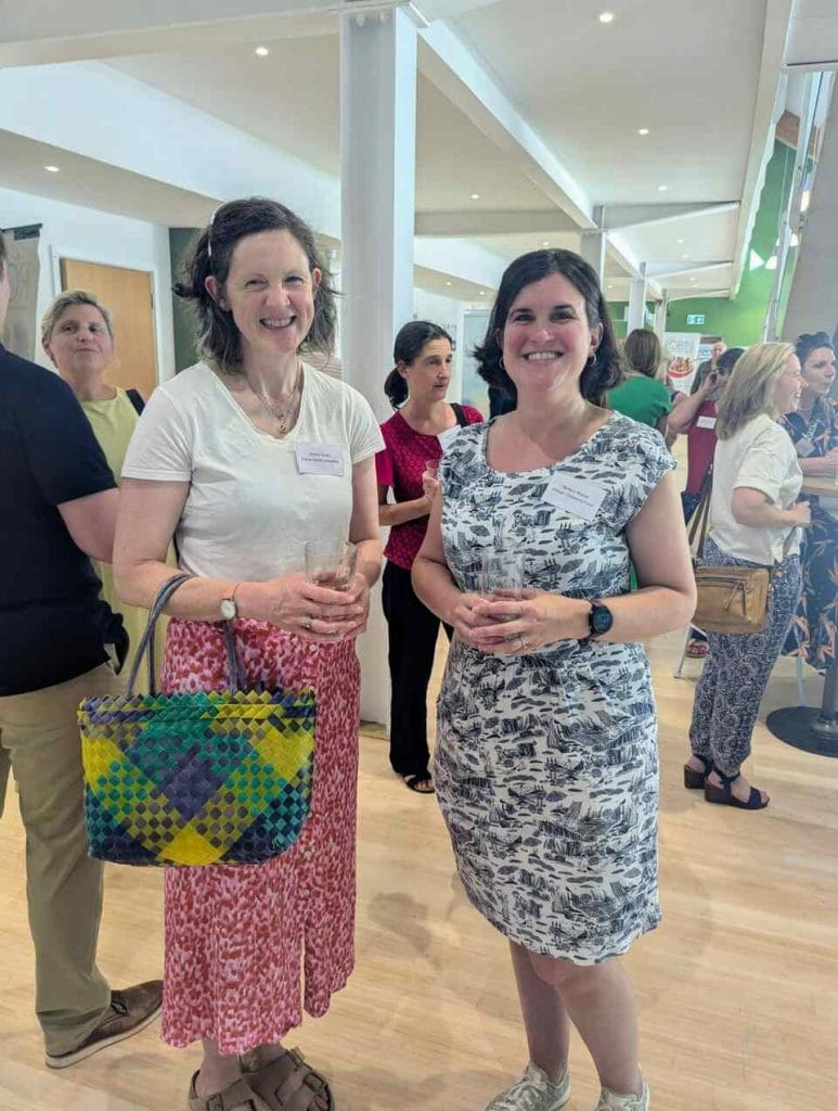 Two women holding gift bags and smiling at a networking event