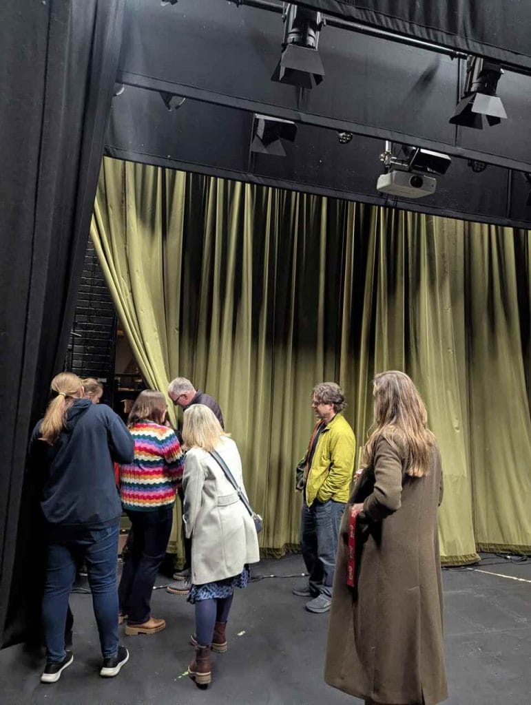 Audience members chatting in front of green stage curtains at a theatre