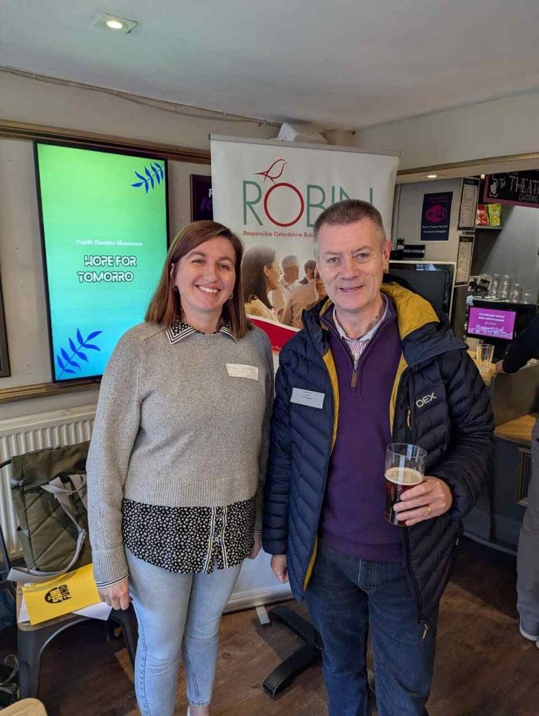 Two attendees standing and talking at a networking event with display screens behind them